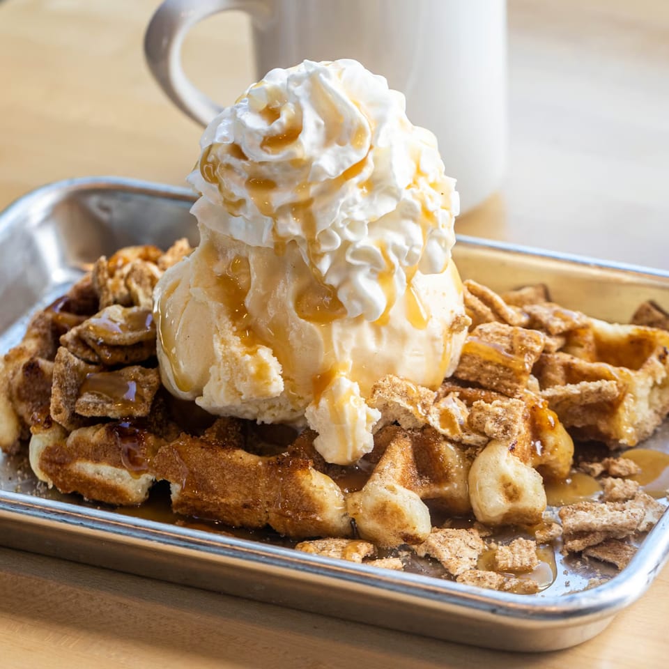 Cinnamon waffle topped with vanilla ice cream, whipped cream, caramel drizzle, and cereal crumbles.